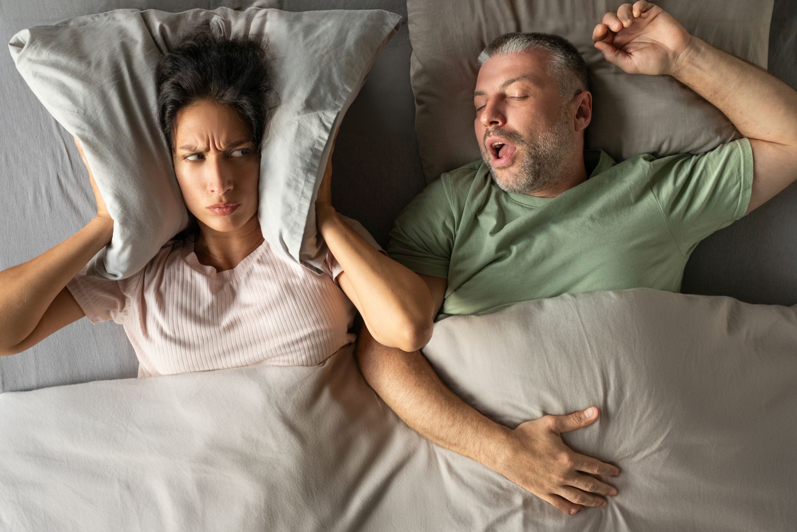 unhappy-tired-woman-covering-her-ears-with-pillow-can-handle-loud-snore-her-husband-top-view Snoring problems - orthodontics solutions